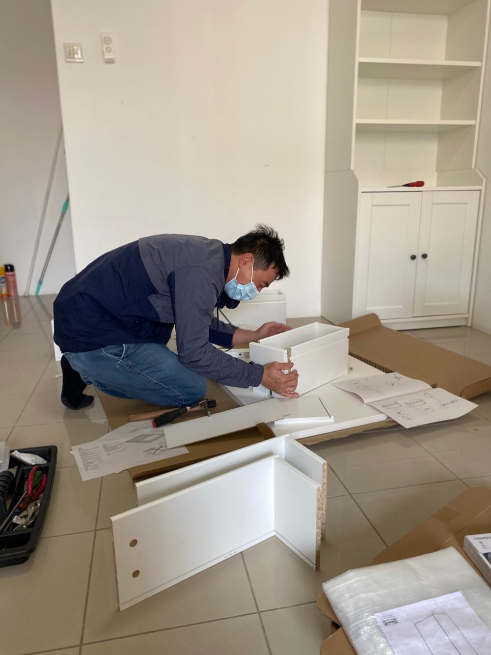 Assembling a white flat-pack drawer unit on a living room floor, with tools and instructions laid out